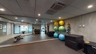 Located at 459 23rd St in Oakland, CA, this well-appointed fitness center offers a comprehensive workout environment across a single floor. The space is divided into distinct functional zones, each designed to support a variety of training styles. The cardio area is lined with floor-to-ceiling windows overlooking the street, flooding the room with natural light while providing an energizing view. It is equipped with multiple treadmills, elliptical trainers, stationary bikes, and a stair climber. Adjacent to the cardio zone is a strength training area featuring a multi-tiered dumbbell rack, kettlebells, medicine balls, resistance equipment, and adjustable weight benches. A dedicated functional training and stretching studio features resilient rubber flooring, full-length wall mirrors, a rack of stability balls in assorted sizes, and wall-mounted medicine balls—ideal for group fitness, stretching, or movement training. Throughout the facility, recessed lighting and ceiling-mounted HVAC units maintain a comfortable, well-lit atmosphere. Glass partitions and clean, neutral-toned walls contribute to an open, modern aesthetic. The rubber flooring used throughout ensures safety and durability. This fitness center is thoughtfully designed to accommodate a wide range of exercise routines in a sleek, urban setting.