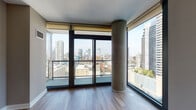 Located in the heart of Chicago's vibrant River North neighborhood at East Illinois Street, this high-rise unit offers a compelling blend of modern design and urban living. The space is defined by dramatic floor-to-ceiling glass windows that wrap around the living area, framing sweeping panoramic views of the Chicago skyline and surrounding cityscape. Exposed concrete columns add an industrial architectural accent, complementing the clean, contemporary aesthetic throughout.

The open-concept living and dining area flows seamlessly into a well-appointed kitchen featuring warm wood cabinetry, granite countertops, a stainless steel appliance suite including a range, microwave, and refrigerator, and a sleek subway tile backsplash. A peninsula island provides additional prep space and casual seating. Track lighting illuminates the kitchen, while light hardwood flooring extends throughout the main living areas.

The bedroom is carpeted for comfort and benefits from its own large floor-to-ceiling window with direct city views and access to a balcony. The bathroom is finished with tile flooring, a wide vanity with dual sinks, a framed mirror, and a full soaking tub. A sliding barn door adds a stylish, space-conscious touch to the interior layout. Natural light floods every corner of this elevated urban retreat.