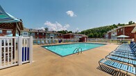Located at 10701 Burkhalter Haas Dr in North Little Rock, Arkansas, this two-floor residential community offers a well-appointed outdoor amenity area centered around a generously sized swimming pool. The pool area serves as a social hub for residents, featuring a broad concrete deck lined with blue lounge chairs and patio seating shaded by colorful umbrellas, providing ample space for relaxation and outdoor recreation.

The community buildings are constructed with classic red brick exteriors accented by neutral trim, and each building rises two floors with balconies that overlook the grounds. A white vinyl fence encloses the pool area, creating a secure and defined outdoor retreat. A poolside clubhouse or amenity structure sits adjacent to the pool, clad in brick with large windows that allow natural light to flow through and views of the pool deck.

The surrounding landscape adds a natural backdrop to the community, with mature tree lines and rolling green hills visible beyond the fence line, contributing to a peaceful, tucked-away atmosphere. The overall setting strikes a balance between community living and natural scenery, making the outdoor pool area a standout feature of this North Little Rock residential property.