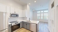 Located at 725–735 Coleman Blvd in Mount Pleasant, South Carolina, this thoughtfully designed unit offers a compact yet functional layout across a single floor. The open-concept living and kitchen area is anchored by a well-appointed kitchen featuring two-tone cabinetry — crisp white upper cabinets paired with soft gray lowers — accented by a white subway tile backsplash and clean white countertops. Stainless steel appliances, including a refrigerator, range, built-in microwave, and dishwasher, give the space a modern, move-in-ready feel. Light wood-tone flooring runs throughout, contributing to a warm, cohesive aesthetic. The living area benefits from natural light through a window overlooking greenery, complemented by a ceiling fan for added comfort. Soaring vaulted ceilings lend an airy, spacious quality that extends the sense of openness well beyond the footprint. The full bathroom is finished in a clean, all-white palette with a tiled tub-shower combo, dark oil-rubbed bronze fixtures, and wood-tone flooring that ties seamlessly to the rest of the unit. A dedicated walk-in closet provides valuable storage. The overall design emphasizes clean lines, bright finishes, and efficient use of space throughout.