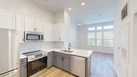Located at 725–735 Coleman Blvd in Mount Pleasant, South Carolina, this thoughtfully designed unit offers a compact yet functional layout across a single floor. The open-concept living and kitchen area is anchored by a well-appointed kitchen featuring two-tone cabinetry — crisp white upper cabinets paired with soft gray lowers — accented by a white subway tile backsplash and clean white countertops. Stainless steel appliances, including a refrigerator, range, built-in microwave, and dishwasher, give the space a modern, move-in-ready feel. Light wood-tone flooring runs throughout, contributing to a warm, cohesive aesthetic. The living area benefits from natural light through a window overlooking greenery, complemented by a ceiling fan for added comfort. Soaring vaulted ceilings lend an airy, spacious quality that extends the sense of openness well beyond the footprint. The full bathroom is finished in a clean, all-white palette with a tiled tub-shower combo, dark oil-rubbed bronze fixtures, and wood-tone flooring that ties seamlessly to the rest of the unit. A dedicated walk-in closet provides valuable storage. The overall design emphasizes clean lines, bright finishes, and efficient use of space throughout.