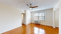 This single-floor unit presents a clean, functional layout designed for comfortable everyday living. The main living area is a standout feature, showcasing warm, polished hardwood flooring that extends throughout the space and reflects natural light generously. A ceiling fan is centrally mounted above, providing both style and airflow. Neutral cream-toned walls create a bright, open atmosphere, while windows fitted with horizontal blinds allow for adjustable natural light and views of the surrounding exterior.

The kitchen is efficiently designed with warm wood cabinetry, dark granite-style countertops, a stainless steel sink, and white appliances including a range, microwave, refrigerator, and dishwasher. Light tile flooring and a window contribute to the kitchen's airy feel.

A spacious walk-in closet offers generous storage with built-in shelving and hanging rods on multiple walls, all finished with the same hardwood flooring found throughout the unit. The bathroom features light tile flooring, a white vanity with cabinetry, and a window that brings in natural light while maintaining privacy.

A wall-mounted HVAC unit ensures climate control, and a textured ceiling is consistent across the living spaces. The unit's entry door opens directly into the main living area, making for a straightforward and accessible floor plan.
