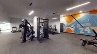Located on Wilshire Boulevard in the heart of Los Angeles, this single-floor fitness center offers a well-appointed and modern workout environment designed to support a full range of exercise activities. The main gym area features durable rubber flooring and is equipped with a functional training cable machine loaded with weight plates, along with an array of cardio equipment including treadmills and elliptical machines with digital displays. Sleek linear pendant lighting illuminates the space from above, complementing the clean white walls. A vibrant abstract mural in orange, blue, and white adds a dynamic, energizing element to the gym floor, giving the space a contemporary and motivating atmosphere. An additional area visible through an open passage offers supplemental workout space with light wood flooring, providing flexibility for varied training needs. A dedicated studio room rounds out the facility, featuring a smooth hardwood floor ideal for group fitness classes, yoga, or dance. This studio is lined with full-length mirrors along one wall, fitted with acoustic panel tiles for sound management, and decorated with a bold geometric mural in teal, yellow, and light blue. Recessed and flush ceiling lights keep the studio bright and functional. Together, these spaces create a comprehensive, thoughtfully designed fitness facility.