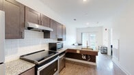 Located at 16790 Chandler Rd in East Lansing, Michigan, this efficiently designed one-bedroom, one-bathroom unit offers a thoughtful layout across a single floor. The open-concept kitchen and living area forms the heart of the space, featuring rich dark-toned shaker cabinetry, granite countertops, white subway tile backsplash, and a full suite of stainless steel appliances including a range, refrigerator, microwave, and dishwasher. Light wood-style flooring runs throughout the main living area, contributing to a bright and clean aesthetic. Sliding glass doors at the far end of the living area allow natural light to flow in and provide outdoor access. The bedroom is a cozy, well-defined retreat with neutral carpet flooring and a window that brings in additional natural light. The full bathroom is designed with accessibility in mind, featuring ADA-compliant grab bars, a wide open layout, wood-look tile flooring, a granite vanity, and a deep soaking tub. A dedicated in-unit laundry area houses a Whirlpool front-loading washer and dryer alongside overhead shelving for added storage. Clean white walls and recessed lighting throughout give the space a modern, well-maintained feel.