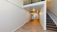 Located at 4154 Roosevelt St in Whitehall, PA, this two-floor unit offers a well-organized layout spread across a spacious main level and a more intimate upper level. The main floor features a long, open floor plan with light wood-tone vinyl plank flooring throughout, baseboard heating, and a ceiling fan. The kitchen is positioned along one wall and is equipped with gray shaker-style cabinetry, white appliances including a refrigerator, electric range, microwave, and dishwasher, as well as a stainless sink — creating a clean, functional workspace. A staircase with a wood handrail and dark metal balusters leads to the upper level, where a loft-style open area offers flexible use of space. This upper floor also includes a dedicated closet and a full bathroom featuring a combination tub and shower with chrome fixtures, a toilet, and wood-look flooring. A wall-mounted mini-split HVAC unit on the upper level provides additional climate control. Black metal railing lines the open stairwell on the upper floor, adding a modern industrial accent. The neutral gray and white color palette, consistent flooring, and clean finishes throughout give the space a fresh, move-in-ready feel.