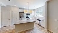 Located at Edgewater Corporate Pkwy in Fort Mill, South Carolina, this two-story residence offers a thoughtfully designed layout with contemporary finishes throughout. The main level features wood-look plank flooring that flows through the entry and living areas, creating a warm, cohesive foundation. Ceiling fans provide comfort in the living spaces, while recessed lighting illuminates the hallways connecting each area.

The kitchen stands out as a highlight of the home, showcasing white cabinetry with sleek hardware, granite-style countertops, a subway tile backsplash, and a central island with pendant lighting overhead. A full suite of stainless steel appliances—including a refrigerator, range, microwave, and dishwasher—completes the space, alongside a built-in wine rack and a window that invites natural light.

The upper level transitions to plush carpeting in the bedrooms. The primary bedroom is generously sized, featuring a tray ceiling with a ceiling fan and multiple windows that fill the room with light. A spacious walk-in closet with multi-tiered wire shelving offers ample storage. The primary bathroom includes a dual-sink vanity with granite countertops and a soaking tub with a tiled surround.