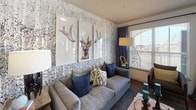 This single-floor residence showcases a cohesive yet eclectic design aesthetic that blends natural textures with bold color choices throughout. The galley-style kitchen is outfitted with white shaker cabinetry, granite-style dark countertops, classic subway tile backsplash, and stainless appliances. A decorative wood panel wall art installation adds a rustic focal point to the space.

The living area features a striking nature-inspired wallpaper with an intricate illustrated pattern, complemented by hardwood flooring and large windows that invite abundant natural light and outdoor views. Seating is comfortable and well-arranged, creating an inviting atmosphere for relaxing or entertaining.

The dining area is positioned near a large window framed by patterned drapery, allowing natural light to fill the space while providing a pleasant outdoor backdrop.

The bedroom is defined by a deep navy blue accent wall, soft carpeting, a ceiling fan, and large windows. A rustic-framed floor mirror adds character to the room.

The full bathroom features dual sinks on a dark granite vanity with white cabinetry, grey subway tile surrounding the tub and shower area, and wood-look flooring, presenting a clean and modern finish throughout.