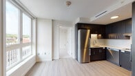 Located at 1500 Hancock Street in Quincy, Massachusetts, this single-floor residence combines modern design with functional living. The open-plan living and kitchen area is anchored by large windows that draw in abundant natural light and offer views of the surrounding neighborhood. Light-toned hardwood-style flooring runs throughout the main living spaces, complementing the clean, neutral walls and creating a bright, airy atmosphere.

The kitchen is a standout feature, outfitted with dark espresso-toned cabinetry extending from counter to ceiling, providing ample storage. Stainless steel appliances include a refrigerator, wall oven, cooktop, and dishwasher, while a white tile backsplash and light countertops create a striking contrast against the dark cabinetry. The layout is efficient and well-organized, suited for everyday cooking and entertaining.

The bedroom is a well-proportioned, quiet space with its own large window overlooking the cityscape, continuing the light hardwood flooring found throughout the unit. The bathroom is thoughtfully designed with accessibility in mind, featuring grab bars, tile flooring, and a clean, minimalist aesthetic. The entry foyer provides a practical transition space with a paneled front door and utility panel access. Overall, the unit presents a cohesive, contemporary living environment.