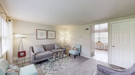 This two-story model unit in Halethorpe, MD offers a well-organized layout spread equally across two floors, connected by a central staircase. The main level features two living areas, a kitchen, and a dining nook, while the upper floor houses both bedrooms, a full bathroom, and a hallway.

The living room is bright and welcoming, with large windows that bring in generous natural light and views of the surrounding greenery. Soft carpeting and neutral wall tones create a calm, versatile atmosphere throughout the space.

The kitchen is fitted with warm oak cabinetry, light countertops, and black appliances including a gas range and refrigerator. A separate dining nook adjacent to the kitchen benefits from a large window, making it an airy spot for casual meals. A closet with bi-fold doors provides additional storage on this level.

Upstairs, the primary bedroom is a comfortable retreat with wide windows, plush carpet, and ample wall space. The second bedroom features carpet flooring and window access to natural light. The shared full bathroom includes a shower/tub combination, light wood-look flooring, and clean white finishes.

Throughout, the unit maintains a consistent, clean aesthetic with light walls, wood-look and carpeted flooring, and practical storage solutions, making it a functional and comfortable two-story home.