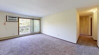 Located at 3359 Coachman Rd in Eagan, Minnesota, this one-bedroom, one-bathroom unit offers a straightforward and functional layout spread across a single floor. The open living area is finished with plush wall-to-wall carpeting, neutral cream-toned walls, and a textured ceiling, creating a clean and understated atmosphere. A large sliding glass door with vertical blinds opens to a private balcony, flooding the living space with natural light and offering views of mature surrounding trees. Baseboard heating runs along the perimeter, ensuring comfortable warmth throughout the colder Minnesota seasons. The kitchen features dark wood cabinetry with ample storage, a granite-style countertop, and wood-look hard flooring, providing a practical workspace that transitions smoothly from the living area. The bedroom is generously sized, with carpeted flooring, a window that brings in natural light and greenery views, a closet with slatted doors, and continued baseboard heating. The full bathroom is finished with tile flooring, a single-sink vanity with warm wood cabinetry, and a full tub-shower combination with a white surround. A hallway connects the main spaces, adding a sense of flow and privacy. This unit offers a comfortable and well-organized living environment in a convenient Eagan location.