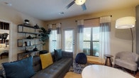 This well-designed single-floor residence offers one bedroom and one bathroom within a thoughtfully arranged layout. The living area is bright and welcoming, featuring wood-style flooring, a ceiling fan, and multiple windows with blinds and two-toned curtains that allow generous natural light. A glass door provides direct access to an outdoor area, enhancing the open feel of the space. An open shelving unit adds functional storage and display space along one wall.

The kitchen is efficiently designed with rich dark-wood cabinetry, a subway tile backsplash, light stone countertops, and a full suite of stainless steel appliances. A kitchen island with a built-in sink and seating for two provides additional prep space and casual dining.

The bedroom offers a calm retreat with plush carpeting, a ceiling fan, and a window with sheer curtains. A bold navy accent wall with vertical wood slat detailing and statement artwork adds a distinctive design touch to the space.

The bathroom features wood-style flooring, dark vanity cabinetry, a stone-topped sink, and a tiled tub-shower combination. The overall aesthetic throughout the residence is modern and cohesive, balancing warm tones with contemporary finishes.