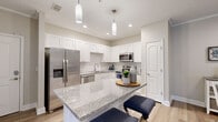 This single-story model residence in Jacksonville, Florida offers a well-designed layout that balances functionality and comfort throughout its thoughtfully arranged rooms. The kitchen serves as a central highlight, showcasing white shaker cabinetry extending to the ceiling, granite countertops, and a large island with seating. Stainless steel appliances, including a French door refrigerator, dishwasher, and microwave, complement the clean, modern aesthetic, while pendant lighting adds a refined touch overhead. Light wood-style flooring runs throughout the main living areas, contributing to a bright, cohesive feel.

The open living room features crown molding, a ceiling fan, and sliding glass doors that allow natural light to fill the space and provide access to an outdoor area. A dedicated dining area with warm neutral tones offers an intimate setting, accented by decorative wall art and a sideboard. Arched architectural details in the hallway add a classic design element connecting the kitchen to the rest of the home.

The bedrooms are carpeted for comfort, each featuring generous closet space and neutral wall tones that create a calm, restful atmosphere. The bathroom includes a full soaking tub with tiled surround. Overall, the residence presents a clean, contemporary interior with consistent finishes throughout.