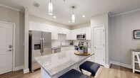 This single-story model residence in Jacksonville, Florida offers a well-designed layout that balances functionality and comfort throughout its thoughtfully arranged rooms. The kitchen serves as a central highlight, showcasing white shaker cabinetry extending to the ceiling, granite countertops, and a large island with seating. Stainless steel appliances, including a French door refrigerator, dishwasher, and microwave, complement the clean, modern aesthetic, while pendant lighting adds a refined touch overhead. Light wood-style flooring runs throughout the main living areas, contributing to a bright, cohesive feel.

The open living room features crown molding, a ceiling fan, and sliding glass doors that allow natural light to fill the space and provide access to an outdoor area. A dedicated dining area with warm neutral tones offers an intimate setting, accented by decorative wall art and a sideboard. Arched architectural details in the hallway add a classic design element connecting the kitchen to the rest of the home.

The bedrooms are carpeted for comfort, each featuring generous closet space and neutral wall tones that create a calm, restful atmosphere. The bathroom includes a full soaking tub with tiled surround. Overall, the residence presents a clean, contemporary interior with consistent finishes throughout.
