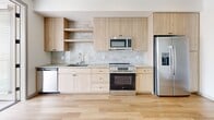Located at 100 S 48th St in Phoenix, Arizona, this efficiently designed studio unit offers a thoughtfully organized single-floor layout that maximizes every square foot. The open living area features light wood-tone flooring throughout, crisp white walls, and a ceiling fan that keeps the space comfortable in the Arizona climate. Large windows with horizontal blinds allow natural light to fill the room, while a glass-paned door provides access to an outdoor balcony area.

The kitchen is a standout feature, outfitted with light wood cabinetry — including both upper enclosed cabinets and open shelving — complemented by a marble-style tile backsplash and neutral countertops. A full suite of stainless steel appliances includes a refrigerator with ice and water dispenser, electric range and oven, built-in microwave, and dishwasher, delivering a highly functional cooking space.

The bathroom continues the modern aesthetic with warm wood-tone vanity cabinetry and durable wood-look flooring. The tub-shower combination is a highlight, featuring large-format marble-patterned tiles extending floor to ceiling, paired with sleek black rod hardware for a contemporary touch.

The bedroom area is bright and airy, with clean white walls and a ceiling fan overhead, offering a calm and restful retreat. This unit presents a clean, modern aesthetic well-suited for urban living in Phoenix.