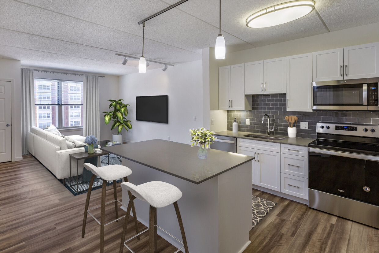 Renovated Package II kitchen with grey quartz countertops, white shaker cabinetry, stainless steel appliances, grey tile backsplash, and hard surface flooring throughout - Avalon Natick