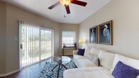 This thoughtfully designed single-floor residence offers a comfortable and functional layout with a warm, neutral color palette throughout. The spacious living room is a standout feature, showcasing vaulted ceilings, a ceiling fan, and rich hardwood-style flooring. Large sliding glass doors flood the space with natural light and provide direct access to an outdoor area with green views, while additional windows keep the interior bright and airy.

The open-plan layout connects the living area to a dedicated dining nook, which features a pendant light fixture and a large window framing lush outdoor scenery. The kitchen is well-equipped with white cabinetry, granite-style countertops, a double basin sink, and white appliances including a refrigerator, stove, and built-in microwave, with convenient access to a laundry area.

The bedrooms are generously sized with plush carpeting, ceiling fans, vaulted ceilings, and ample closet space, offering a serene and restful atmosphere. The bathroom features a long vanity with stone-look countertops, white cabinetry, hardwood-style flooring, and a separate shower and toilet area. Throughout the residence, clean lines and consistent finishes create a cohesive and inviting living environment.