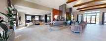 This impressive 4,390 square foot single-story space in Pflugerville, Texas, offers a blend of modern design and comfort. The interior is characterized by an open floor plan that creates a sense of spaciousness and flow. High ceilings with exposed wooden beams add warmth and architectural interest, while large windows flood the area with natural light.

The space is divided into multiple functional areas, including a welcoming lobby, comfortable seating zones, and what appears to be a communal work or dining area. A striking feature is the use of room dividers - sleek, dark-colored pillars with vertical slats that provide subtle separation without compromising the open feel.

The color palette is predominantly neutral, with warm terracotta accent walls adding depth and interest. Furnishings are modern and inviting, featuring a mix of plush seating options in muted tones. Greenery is strategically placed throughout, bringing a touch of nature indoors.

Flooring appears to be polished concrete or large-format tiles, lending a contemporary feel while providing durability for high-traffic areas. Lighting is thoughtfully designed, with a combination of recessed lights, wall sconces, and decorative pendant fixtures.

The space includes smaller, more intimate areas as well, such as a glass-enclosed meeting room and what seems to be a compact workstation nook with a unique, artistic wall treatment. Overall, this versatile space appears designed to foster community interaction, relaxation, and productivity in a stylish, contemporary setting.