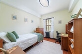 This 130 square foot studio apartment, located at 2295 Piedmont Ave in Berkeley, CA, offers a well-designed living space in a prime location. The room, which serves as both bedroom and study area, is efficiently laid out to maximize the compact footprint. 

The space features warm wooden flooring that complements the cream-colored walls, creating a bright and inviting atmosphere. A large window with sheer curtains allows ample natural light to flood the room, enhancing the sense of spaciousness. The window is equipped with both blinds and a radiator beneath, providing options for light control and heating.

The furnishings are thoughtfully selected for functionality and style. A comfortable single bed with white linens and a textured throw occupies one corner. Adjacent to the bed is a wooden nightstand, offering convenient storage. A sizeable wooden dresser provides additional storage space, while a desk and ergonomic chair create a dedicated study area.

Built-in shelving units offer plentiful storage and display options, perfect for books and personal items. The room also includes a closet for clothing storage. Artwork adorns the walls, adding personality to the space.

The entrance features a solid wooden door with modern electronic lock, ensuring security and convenience. Despite its compact size, this studio apartment efficiently combines living, sleeping, and studying areas, making it an ideal choice for students or young professionals in the Berkeley area.
