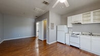 This single-floor studio offers an efficient, open layout that seamlessly combines the kitchen and living area into one cohesive space. Rich hardwood flooring extends throughout, complementing the cool gray walls that lend the interior a clean, modern feel. A ceiling fan overhead provides both light and airflow to the main living area.

The kitchen is positioned along one wall and is well-equipped with white cabinetry, an electric range, a full-size refrigerator, and a sink with light granite-toned countertops. Upper cabinets, including open shelving, offer practical storage, while the layout keeps everything within easy reach. An electrical panel is conveniently located nearby.

The living area benefits from natural light streaming through two narrow windows fitted with white blinds, keeping the space bright yet private. The open floor plan allows for flexible furniture arrangements to suit a variety of living needs.

The bathroom is neatly appointed with hardwood-style flooring, a single-sink vanity with a speckle-top countertop, a toilet, and a full bathtub with shower. A mirrored medicine cabinet above the vanity adds functional storage. A dedicated closet rounds out the unit, providing additional organization space. Overall, the studio presents a straightforward, well-maintained environment ideal for efficient, comfortable living.