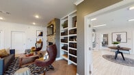 Located on Outer Loop in Louisville, Kentucky, this single-floor community clubhouse is thoughtfully designed to provide residents with a welcoming and functional gathering space. The bright, open entry foyer greets visitors with large glass doors, light tile flooring in a herringbone pattern, and curated wall art, setting an inviting tone throughout.

The lounge area serves as the heart of the space, anchored by a striking floor-to-ceiling brick fireplace with a mounted flat-screen TV above. Built-in white bookshelves filled with books flank the fireplace, while stylish egg-style leather chairs and a patterned area rug complete the cozy, residential atmosphere. Crown molding and recessed lighting add refined architectural detail.

The full kitchen is equipped with stainless steel appliances, white shaker cabinetry, a tiled backsplash, and a large granite-topped island with bar seating beneath a pair of globe pendant lights. Natural light filters in through multiple windows, brightening the space throughout the day.

Adjacent dining areas offer both high-top table seating and standard table arrangements, ideal for casual gatherings or remote work. A private office nook features built-in white cabinetry, a dedicated workspace, and seating for two, anchored by a bold black-and-white abstract artwork. The consistent herringbone flooring and cohesive color palette tie every area of this community space together seamlessly.