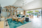Located in the Bixby Village community of Long Beach, California, this single-story clubhouse combines contemporary coastal design with functional, well-appointed communal spaces. The grand entry foyer sets an immediate tone with soaring vaulted ceilings, a striking geometric tile accent wall in layered tones of gray and beige, and large transom windows that flood the space with abundant natural light. Light wood-look tile flooring runs throughout, lending warmth and continuity across all areas.

Just inside, a curved reception desk is flanked by mailbox banks, package lockers, and pendant lighting, offering a polished and practical welcome hub for residents. Beyond, a vibrant workspace or common room features bold teal cabinetry, stainless steel drawers, and a wide window overlooking the outdoor pool area.

The expansive main lounge is a standout, boasting dramatic vaulted ceilings, a ceiling fan, a sleek black fireplace with wall-mounted TV, built-in bench seating, and an open-concept layout that accommodates both dining and lounging. Large folding glass doors open the lounge directly onto a covered pergola terrace and resort-style pool deck, complete with lounge chairs and umbrella-shaded seating—seamlessly blending indoor and outdoor living in true Southern California fashion.