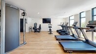 Located at 95 Plum Nelly Circle in Nashville, TN, this well-appointed fitness center offers a clean, modern environment designed to support a comprehensive workout routine. The single-level space features warm hardwood-style flooring throughout, crisp white walls, and recessed lighting that creates a bright and welcoming atmosphere.

The cardio area is outfitted with a row of TRUE brand treadmills and ellipticals, complemented by smart stationary bikes and a rowing machine, all positioned to take advantage of the natural light streaming in through large windows that frame views of the surrounding community. A wall-mounted flat-screen television enhances the cardio experience.

The strength training section includes a full rack of dumbbells ranging across multiple weight increments, adjustable workout benches, and a selectorized strength machine for targeted muscle training. A TRUE cable pulley system anchors one side of the room, offering versatile resistance training options.

Large glass doors with dark steel frames on one end of the space provide a sense of openness and connectivity to the exterior, while also allowing additional natural light to filter in. The overall design is minimal and functional, prioritizing ease of movement and a distraction-free environment suited for focused training sessions.