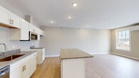 Located at Camden in Scarborough, Maine, this thoughtfully designed one-bedroom, one-bathroom residence offers a comfortable and modern living experience on a single floor. The open-concept kitchen and living area serves as the heart of the home, showcasing light hardwood-style flooring, recessed lighting, and a neutral warm-toned color palette that creates a bright and welcoming atmosphere. The kitchen is outfitted with crisp white shaker cabinetry, granite countertops, stainless steel appliances including a dishwasher and microwave, and a central island with matching granite that provides additional prep and seating space. The spacious living area benefits from large sliding glass doors that open to an outdoor view of the surrounding neighborhood, flooding the room with natural light. A wall-mounted mini-split unit provides efficient climate control. The bedroom is generously sized, featuring two large windows that frame views of the community and surrounding landscape, along with the same warm hardwood-style flooring. The bathroom is finished with a granite-topped white vanity, tile flooring, and a walk-in shower. Clean lines and consistent finishes throughout lend the space a cohesive, move-in-ready appeal.