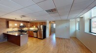 This single-floor space combines industrial charm with modern updates, creating a functional and visually distinctive environment. Warm hardwood floors extend throughout, complemented by drop-panel ceilings and neutral wall tones that provide a clean, versatile backdrop.

The kitchen is a standout feature, offering rich wood cabinetry, dark granite-style countertops, a central island with pendant lighting, and a full suite of stainless steel appliances including a range, microwave, dishwasher, and refrigerator. A brick accent wall adds a striking industrial element to the kitchen and adjacent living area, lending the space a unique character rarely found in modern units.

The open living and dining area is generously proportioned, with natural light filtering in through multiple windows that frame views of surrounding greenery. The exposed brick wall in the main living space further reinforces the building's historic character.

Private rooms include well-sized spaces with windows, hardwood floors, and built-in closet organizers for practical storage. The bathroom features a wood-framed vanity mirror, granite-topped vanity, and a full shower-tub combination.

A utility area with laundry is also present, adding everyday convenience. Overall, this space offers a compelling mix of character, comfort, and functionality.