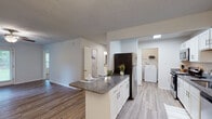 This single-story unit at 6430 Brookstone Ln in Fayetteville, NC offers a well-designed layout with a cohesive, updated aesthetic throughout. The kitchen serves as a functional centerpiece, featuring crisp white shaker-style cabinetry, granite countertops, and a full suite of appliances including a stainless steel refrigerator, electric range, microwave, and dishwasher. A peninsula with additional granite counter space connects the kitchen to the adjacent dining area, which is accented by a elegant chandelier. A dedicated laundry area with a full-size washer is conveniently accessible directly from the kitchen. Light wood-style vinyl flooring runs through the main living and kitchen areas, while plush carpeting lines the bedrooms. The living room is equipped with a ceiling fan and receives natural light through window blinds. Two well-proportioned bedrooms offer comfortable retreats, each carpeted and naturally lit. The bathrooms mirror the kitchen's design language with matching granite countertops, white cabinetry, brushed nickel hardware, and large vanity mirrors. Textured ceilings and neutral wall tones carry throughout, creating a clean, consistent atmosphere across the entire unit.