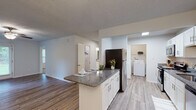 This single-story unit at 6430 Brookstone Ln in Fayetteville, NC offers a well-designed layout with a cohesive, updated aesthetic throughout. The kitchen serves as a functional centerpiece, featuring crisp white shaker-style cabinetry, granite countertops, and a full suite of appliances including a stainless steel refrigerator, electric range, microwave, and dishwasher. A peninsula with additional granite counter space connects the kitchen to the adjacent dining area, which is accented by a elegant chandelier. A dedicated laundry area with a full-size washer is conveniently accessible directly from the kitchen. Light wood-style vinyl flooring runs through the main living and kitchen areas, while plush carpeting lines the bedrooms. The living room is equipped with a ceiling fan and receives natural light through window blinds. Two well-proportioned bedrooms offer comfortable retreats, each carpeted and naturally lit. The bathrooms mirror the kitchen's design language with matching granite countertops, white cabinetry, brushed nickel hardware, and large vanity mirrors. Textured ceilings and neutral wall tones carry throughout, creating a clean, consistent atmosphere across the entire unit.