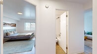Located at 2175 NW Davis St in Portland, Oregon, this one-bedroom, one-bathroom unit offers a well-organized layout across a single floor. The space is designed for efficient, comfortable living, with each room thoughtfully arranged to maximize functionality.

The bedroom is a generously proportioned retreat featuring light wood flooring, a large window that invites natural light and neighborhood views, and clean white walls that create a bright, airy atmosphere. A full-length mirror and warm mid-century-style furnishings complement the room's understated, modern character.

The kitchen is outfitted with white cabinetry providing ample storage, a stainless steel sink, a full-size refrigerator, and a coil-top range. Light wood-tone flooring extends through the space, contributing to a cohesive, clean aesthetic throughout.

The bathroom features a wide vanity with dual mirrors and built-in lighting, white cabinetry below offering practical storage, and a combined shower and tub enclosure finished in white tile. The overall design is clean and utilitarian.

A hallway connects the rooms, maintaining a logical and accessible flow through the unit. Throughout the space, the consistent use of white walls, light flooring, and natural light creates a cohesive, bright environment well-suited for everyday living in the heart of Portland's NW neighborhood.