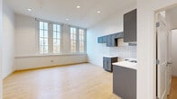 Located at 25 Public Square in Willoughby, Ohio, this one-bedroom, one-bathroom unit offers a thoughtfully designed single-floor layout. The open-concept kitchen and living area serves as the heart of the space, featuring light hardwood flooring, white walls, and recessed lighting that create a bright, airy atmosphere. Large multi-pane windows flood the living area with natural light and offer pleasant views of the surrounding greenery. The kitchen is equipped with slate-blue shaker-style cabinetry, white quartz countertops, a stainless steel dishwasher, a undermount sink, and a full subway tile backsplash, with an island unit providing additional prep and storage space. The elevated ceiling height throughout adds a sense of openness. The bathroom is finished with classic penny-round mosaic tile flooring, a walk-in glass-enclosed shower with white subway tile walls, navy accent tile, built-in shelving, and a vanity with matching cabinetry. The bedroom is a comfortable, private retreat with the same warm hardwood flooring found throughout. Additional spaces include a dedicated laundry area, a utility room, a hallway, and a closet, maximizing functionality within the overall footprint.