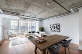 This well-designed one-bedroom, one-bathroom unit offers an efficient layout across a single floor, making effective use of its compact footprint. The living area is characterized by warm hardwood flooring and crisp white walls, creating a clean, modern aesthetic throughout. Large floor-to-ceiling glass panels and sliding doors dominate the main living space, flooding the interior with natural light and providing views of the surrounding urban building facade.

The bedroom is a comfortably sized private retreat, also featuring hardwood flooring and large windows that continue the unit's bright, airy character. White walls and simple finishes keep the space feeling open and uncluttered.

The kitchen area, visible in the unit's layout, is equipped with stainless steel appliances — including a refrigerator and range — set against white cabinetry and light countertops, providing practical functionality within the compact space.

The bathroom is a standout feature, showcasing floor-to-ceiling marble-effect porcelain tile walls and a mosaic tile shower floor. A frameless glass shower enclosure paired with matte black fixtures, including a wall-mounted showerhead and controls, adds a refined, contemporary touch. The overall design of the unit balances modern finishes with practical, efficient use of space.