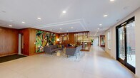 Located at 114 Forrest Ave in Narberth, PA, this single-floor commercial space offers a sophisticated and welcoming environment across a generous footprint of six distinct areas. Guests are greeted by a striking entryway framed by black-steel-and-glass doors, setting an elegant tone that carries throughout the interior.

The main lobby is anchored by rich warm-toned wood wall paneling, large-format light tile flooring, and recessed lighting that creates a bright, polished atmosphere. A vibrant, large-scale botanical mural serves as a dramatic focal point, complementing the curated seating area of contemporary gray sofas and chairs arranged around a central coffee table on a textured area rug.

A freestanding open wood shelving unit acts as a refined divider, separating the main lounge from an additional seating nook furnished with modern high-back lounge chairs and a bold yellow floor lamp. This secondary lounge benefits from abundant natural light through large windows overlooking the surrounding neighborhood.

A glass-walled conference room, enclosed by matching black-steel-framed partitions, provides a professional meeting space visible from the entry corridor, offering both transparency and function.

Ambient blue accent lighting highlights an architectural ceiling tray detail, adding a contemporary and dynamic touch. Throughout, the consistent use of wood accents, clean lines, and carefully selected furnishings creates a cohesive, upscale, and inviting commercial environment.