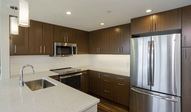 Open kitchens with stainless steel appliances, ample quartz countertop space, and French door refrigerator - Park Towne Place Apartments