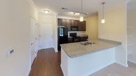 Located at 300 Cormorant Place in Frederick, Maryland, Unit 1301 is a thoughtfully designed single-floor residence that combines modern finishes with functional living spaces. The open-concept kitchen serves as a central highlight, featuring rich dark-toned cabinetry, granite countertops, a double-basin sink, and pendant lighting that adds a stylish touch. Black appliances, including a refrigerator, range, and built-in microwave, complete the kitchen's sleek aesthetic. A peninsula with granite counters seamlessly connects the kitchen to the living area, which is finished with hardwood-style flooring and crown molding for an elevated feel. Track lighting further enhances the kitchen and dining areas. The bedroom offers plush carpeting, a ceiling fan, and a window with views of the surrounding greenery, filling the room with natural light. The bathroom is well-appointed with a granite-topped dark vanity, hardwood-style flooring, and convenient access to a walk-in closet, providing ample storage. Crown molding details are carried throughout the main living areas, lending a cohesive and polished character to the entire residence. The layout flows naturally from entry to living spaces, making the unit both comfortable and practical.