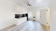 Located at 744 Beacon Avenue in Los Angeles, this efficiently designed single-floor unit offers a thoughtful layout across a compact footprint. The open main area seamlessly connects the kitchen and living space, bathed in natural light from multiple windows fitted with blinds. The kitchen is a standout feature, boasting dark granite countertops with subtle speckled detailing, bold black subway tile backsplash, white shaker-style cabinetry with brushed nickel hardware, a stainless steel undermount sink, and a full-size stainless steel refrigerator. A ceiling fan overhead aids in climate comfort alongside a wall-mounted heating unit. Light wood-style luxury vinyl plank flooring runs throughout, lending a clean, contemporary feel to the space. The bedroom, though cozy, includes a built-in closet with a full-length hanging rod and shelving, maximizing storage efficiency. The bathroom is neatly appointed with a walk-in shower stall, pedestal sink with mirror cabinet, and a toilet, all set against crisp white walls and matching flooring. Clean white walls throughout the unit create a bright, airy ambiance that makes the space feel open and welcoming.