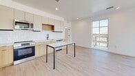 Located at 610 S 400 W in Salt Lake City, Utah, this modern 2-bedroom, 2-bathroom residence offers a thoughtfully designed layout with contemporary finishes throughout. Light wood-tone flooring flows seamlessly across the entire space, complementing the clean white walls and creating a bright, cohesive aesthetic.

The open-concept kitchen and living area serves as the heart of the home. The kitchen features light wood cabinetry, white subway tile backsplash, stainless steel appliances including a dishwasher, microwave, and range, and a central island with a white countertop — ideal for dining or food preparation. Large floor-to-ceiling windows and a sliding glass door connect the living area directly to a private balcony, offering sweeping views of the Salt Lake City skyline and surrounding Wasatch Mountains.

The primary bedroom is a well-proportioned retreat with generous natural light and direct balcony access through expansive glass doors framing the same striking mountain panorama. Both bedrooms include dedicated closet spaces with black metal clothing rods. Two full bathrooms serve the residence — one featuring a tiled soaking tub and shower combination with matte black fixtures, and the other a glass-enclosed walk-in shower with a wood-toned vanity. A dedicated laundry area houses a stacked washer and dryer for added convenience.