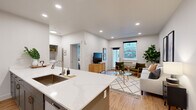 This thoughtfully designed one-bedroom, one-bathroom residence offers an efficient and modern layout across a single floor. The open-concept kitchen and living area serves as the heart of the home, anchored by a generous quartz-topped island with an undermount sink and seating for multiple stools — ideal for casual dining or entertaining. The kitchen features tall gray shaker-style cabinetry, stainless steel appliances including a full-size refrigerator and built-in microwave, and recessed lighting throughout. Light hardwood flooring flows seamlessly from the kitchen into the living area, which is bright and welcoming with a large window that brings in natural light and views of the surrounding neighborhood. The bedroom offers a comfortable, serene retreat with direct access to a dedicated closet with built-in shelving. The full bathroom is finished with clean, neutral tones, featuring a tub-shower combination with brushed nickel fixtures, a gray vanity with white countertop, and wood-look flooring. A in-unit laundry closet houses a full-size washer and dryer with overhead shelving for storage. Recessed lighting and a crisp white color palette create a bright, modern ambiance throughout the entire space.