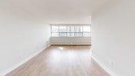 Located at 65 Thorncliffe Park Dr in Toronto's Thorncliffe Park neighbourhood, this one-bedroom, one-bathroom unit offers a well-organized layout across a single floor. Light hardwood-style flooring runs throughout the main living areas, contributing to a clean, cohesive aesthetic.

The living room is generously proportioned, featuring a wide bank of floor-to-ceiling windows that flood the space with natural light and provide open views of the surrounding neighbourhood. Baseboard heating runs along the perimeter, and the room connects seamlessly to the private balcony, extending the living space outdoors.

The galley-style kitchen is efficiently designed with white shaker cabinetry lining both sides, granite-style countertops, stainless steel appliances including a refrigerator and electric range, and a stainless steel sink. A window at the end of the kitchen brings in additional natural light.

The bedroom is a comfortable size, featuring its own window, baseboard heating, and neutral walls that offer a calm, restful environment. The full bathroom is finished with large-format grey stone-look wall tiles surrounding the bathtub and shower combination, complemented by chrome fixtures. A hallway connects all areas of the unit, providing a practical and well-structured flow throughout the space.