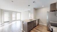 Located at 555 W 5th Ave in Columbus, Ohio, this thoughtfully designed 2-bedroom, 2-bathroom residence offers a modern living experience across a single floor. The open-concept layout seamlessly connects the kitchen, dining, and living areas, creating an airy and functional space bathed in natural light from large windows with horizontal blinds.

The kitchen is a standout feature, showcasing a granite-topped island with an undermount sink and a sleek linear pendant light overhead. Dark wood cabinetry, a subway tile backsplash, and a full suite of stainless steel appliances — including a refrigerator, range, and microwave — complete this well-appointed space. Light wood-style flooring extends through the main living areas, adding warmth and continuity.

The living room is bright and open, with wide windows and a glass-panel door that invite natural light throughout the day. Both bedrooms feature plush carpeting and generous window coverage offering outdoor views. Each bedroom is served by its own dedicated closet.

The two bathrooms are finished with large-format tile flooring, granite-topped white vanities, and brushed nickel fixtures. One bathroom features a soaking tub with shower, while the other offers a glass-enclosed shower stall. Neutral tones throughout create a clean, contemporary ambiance.