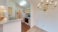 This single-floor residence offers a functional and well-organized layout designed for comfortable everyday living. The open-concept living area is bright and airy, featuring vaulted ceilings, plush neutral carpeting, and a ceiling fan with a light fixture. Natural light filters in through multiple windows, while a door provides convenient exterior access. An elegant gold chandelier marks the transition into the dining area, which connects seamlessly to the kitchen.

The galley-style kitchen is thoughtfully designed with light wood cabinetry offering ample storage, a double stainless steel sink with laminate countertops, a white refrigerator, and an electric range. A peninsula-style counter creates a natural separation from the living and dining spaces while maintaining an open feel. Hardwood-style flooring runs throughout the kitchen, adding warmth and durability. A utility access panel is visible near the kitchen's rear entry.

The bedroom is generously sized, carpeted, and equipped with a ceiling fan. A large walk-in closet with built-in shelving provides excellent storage. A window allows for natural light and ventilation. The bathroom features a clean, all-white tub and shower combination with chrome fixtures, set against smooth white wall surrounds for a simple, practical finish.