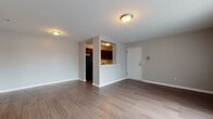 This single-floor unit offers a practical and well-designed layout across several distinct areas. The open living space is finished with wood-style plank flooring and neutral gray walls, creating a clean, versatile environment. Flush-mount ceiling fixtures provide consistent overhead lighting throughout. A pass-through opening connects the living area to the kitchen, enhancing the sense of openness between the two spaces.

The kitchen is outfitted with rich dark wood cabinetry, marble-patterned countertops, and a classic white subway tile backsplash. Black appliances, including a gas range with overhead ventilation and a full-size refrigerator, complement the darker tones of the cabinetry. A stainless steel sink with a window-side position completes the functional workspace.

The bathroom features floor-to-ceiling large-format tile in a warm gray marble pattern surrounding a soaking tub, paired with a white vanity and mirrored medicine cabinet.

Bedrooms vary in finish—one features wood-style flooring and large vertical-blind-covered windows allowing generous natural light, while another is carpeted with a window and baseboard heating unit. The floor plan reveals a compact yet efficiently organized layout that maximizes usable space throughout.
