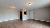 This single-floor unit offers a practical and well-designed layout across several distinct areas. The open living space is finished with wood-style plank flooring and neutral gray walls, creating a clean, versatile environment. Flush-mount ceiling fixtures provide consistent overhead lighting throughout. A pass-through opening connects the living area to the kitchen, enhancing the sense of openness between the two spaces.

The kitchen is outfitted with rich dark wood cabinetry, marble-patterned countertops, and a classic white subway tile backsplash. Black appliances, including a gas range with overhead ventilation and a full-size refrigerator, complement the darker tones of the cabinetry. A stainless steel sink with a window-side position completes the functional workspace.

The bathroom features floor-to-ceiling large-format tile in a warm gray marble pattern surrounding a soaking tub, paired with a white vanity and mirrored medicine cabinet.

Bedrooms vary in finish—one features wood-style flooring and large vertical-blind-covered windows allowing generous natural light, while another is carpeted with a window and baseboard heating unit. The floor plan reveals a compact yet efficiently organized layout that maximizes usable space throughout.