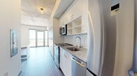 This efficiently designed studio offers a thoughtful single-floor layout that maximizes every inch of its compact footprint. The combined kitchen and living area serves as the heart of the space, featuring hardwood-style flooring that runs throughout and a bright, open feel enhanced by a striking set of floor-to-ceiling glass French doors. These doors flood the living area with natural light and frame panoramic views of the surrounding cityscape and the waterfront beyond — a standout feature of the unit.

The galley-style kitchen is well-appointed with white cabinetry that extends to the ceiling for maximum storage, a classic white subway tile backsplash, granite countertops, and a full suite of stainless steel appliances including a refrigerator, range, built-in microwave, and dishwasher. A wall of built-in storage cabinetry adjacent to the kitchen adds further functionality to the space.

The bathroom continues the clean, modern aesthetic with white vanity cabinetry, matching granite countertops, a large mirror, and hardwood-style flooring. A wall-mounted mini-split HVAC unit provides efficient climate control throughout the space. Exposed concrete ceiling details lend an industrial character, complementing the overall contemporary design of this streamlined urban studio.