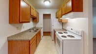 This single-floor unit at 2530 14th St S in Fargo, North Dakota, offers a practical and straightforward layout designed for comfortable everyday living. The interior features a consistent design language throughout, with warm-toned oak doors and trim complementing neutral white walls and textured popcorn ceilings.

The galley-style kitchen is well-equipped, featuring abundant warm oak cabinetry on both sides, granite-look countertops, a double stainless steel sink, and white appliances including an electric range and refrigerator. Light vinyl flooring and a flush ceiling fixture keep the space bright and easy to maintain. A doorway at the end of the kitchen connects to additional areas of the unit.

The living area is carpeted and includes a ceiling fan, with a half-wall partition adding subtle definition to the space. Bedrooms are also carpeted and equipped with baseboard heating units and windows that allow natural light. One bedroom features a wide horizontal window with vertical blinds, while another offers a standard window with blinds.

A hallway connects the main rooms and provides access to the bathroom, which includes a wood-vanity cabinet, white countertop, mirror, and light vinyl flooring. The corridor features flush ceiling lighting and warm wood-toned doors throughout, maintaining a cohesive and functional aesthetic across the entire unit.
