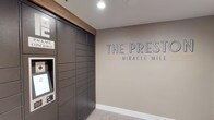 The Preste Miracle Mile presents a thoughtfully designed lobby and common area that combines functionality with clean, contemporary aesthetics. The entrance area immediately establishes the building's identity through prominent branded signage displayed on a warm taupe accent wall, complemented by recessed lighting and light-toned tile flooring that runs throughout the space.

A key feature of the lobby is the floor-to-ceiling automated package locker system, finished in dark charcoal and equipped with an interactive touchscreen terminal, offering residents a secure and convenient solution for parcel retrieval. Adjacent to this, a wall-mounted mailbox unit provides individual compartments for traditional mail delivery.

The elevator vestibule is clean and functional, featuring stainless steel elevator doors framed by neutral gray walls and accented by a distinctive slatted wood panel detail that adds warmth and texture to the otherwise minimalist corridor. A wall-mounted monitor displaying building information serves as a practical communication hub for residents.

Overall, the common areas of The Preste Miracle Mile reflect a modern residential aesthetic, balancing practical amenities with refined design details that create a welcoming and organized environment for residents.