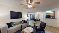 Located at 1700 Woodbury Rd in Orlando, Florida, this single-story residence offers a well-designed, open-concept floor plan that seamlessly connects the living, dining, and kitchen areas. The living room features light wood-style flooring, a ceiling fan with light fixture, and large windows that allow natural light to fill the space. The open layout flows directly into a dedicated dining area and a convenient in-unit laundry space visible in the background.

The kitchen is outfitted with warm honey-toned wood cabinetry, granite-style countertops, black appliances including an electric range and dishwasher, and a mosaic tile backsplash that adds visual texture to the space.

Both bedrooms are carpeted and well-proportioned, each featuring windows with outdoor views and ceiling details. One bedroom includes space for a work desk, making it functional as both a sleeping and office area.

The two bathrooms mirror each other in design, each featuring wood-toned vanity cabinetry, wide countertops, large mirrors, and light wood-style flooring. The layouts are clean and practical, with shower-tub combinations and ample storage.

Overall, this residence provides a comfortable and functional living environment with a cohesive design aesthetic throughout, situated in the East Orlando area of Florida.