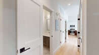 Located at 181 Freeman Ave in Islip, NY, this contemporary two-floor residence offers a thoughtfully designed interior with modern finishes throughout. The kitchen is a standout feature, showcasing a two-tone design with crisp white upper cabinetry and warm wood-toned lower cabinets, complemented by quartz countertops, a subway tile backsplash, and a full suite of stainless steel appliances. A peninsula with pendant lighting adds both function and style, opening to the main living area with light hardwood flooring that flows seamlessly throughout the first floor. A half bath with a wood-accented vanity and marble-style tile flooring is conveniently located off the main hallway. The upper level features generously sized rooms with soft carpeting, neutral walls, and ample natural light from multiple windows dressed with blinds. One room opens to a walk-in closet, while a spacious open area with hardwood floors and a bank of windows offers flexible use. The bathrooms are elegantly appointed, with one featuring a large glass-enclosed walk-in shower clad in marble-look tile with contrasting accent banding. Recessed lighting, clean white trim, and a consistent modern aesthetic tie the entire space together with a fresh, move-in-ready appeal.