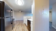 This efficient and thoughtfully laid-out one-bedroom, one-bathroom unit offers a comfortable living experience across a single floor. The open-concept kitchen and living area serves as the heart of the unit, with the kitchen featuring white shaker-style cabinetry, white countertops, black appliances including a refrigerator, electric range, and dishwasher, and warm wood-tone luxury vinyl plank flooring that extends throughout the main living space. A ceiling fan with light fixture adds both comfort and functionality to the combined living area. A large sliding glass door floods the living room with natural light and opens to a private balcony overlooking a lush, tree-lined landscape. The living room is finished with plush carpeting and a textured ceiling. The bedroom offers comfortable proportions, soft carpeting, and a spacious closet with bifold doors and a full-length hanging rod for ample storage. A wall-mounted heating and cooling unit ensures year-round climate control. The bathroom is clean and functional, featuring a single vanity with a light countertop, a mirrored medicine cabinet, built-in shelving, and a full tub-shower combination. Overall, the unit presents a clean, neutral palette with practical finishes throughout.